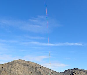 A small boat hanging beneath a helicopter near an Antarctic lake.