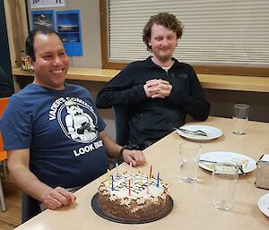 Two men sitting at a table with a birthday cake