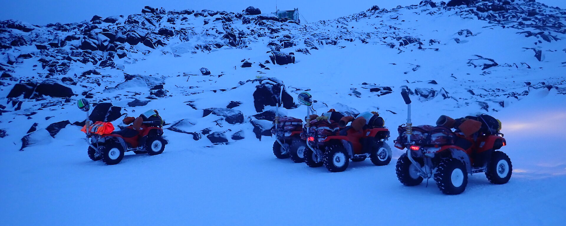 four quad bikes in front of a landscape of snow and rocks