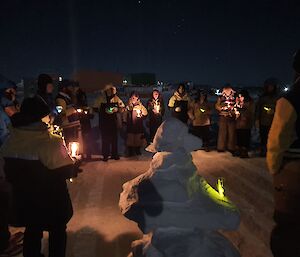 Group of expeditioners standing in a circle holding candles at night