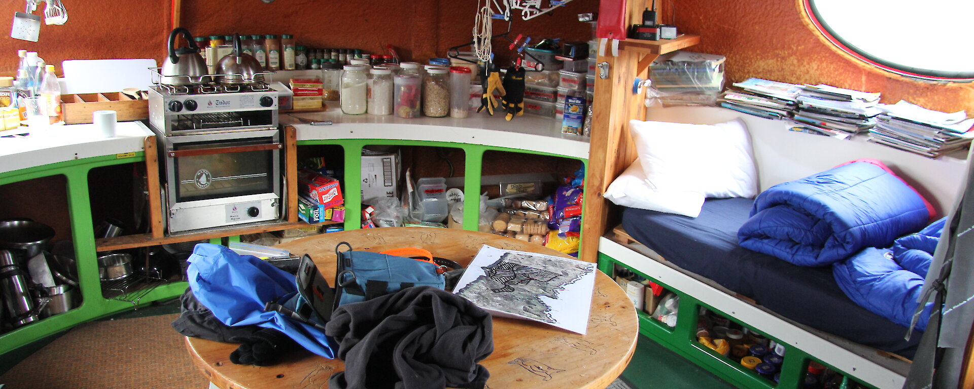 Inside the small googie hut, showing a round table, chairs, stove and kitchenalia.