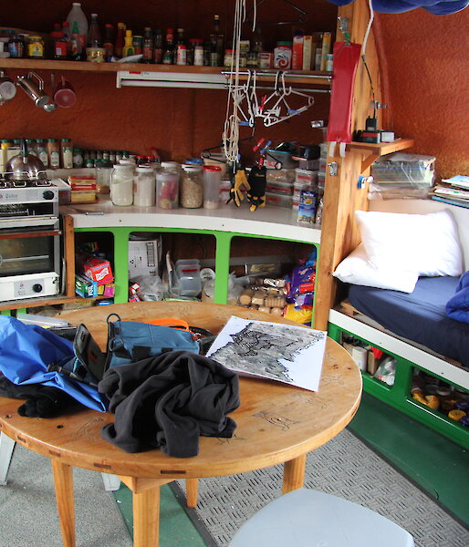 Inside the small googie hut, showing a round table, chairs, stove and kitchenalia.