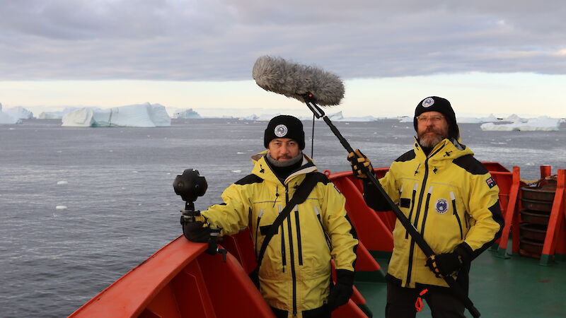 John McCormick holds a 360 degree camera and Adam Nash holds a boom microphone, on the deck of the Aurora Australis in Antarctica.