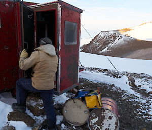 An expeditioner inspecting the condition of a field hut door