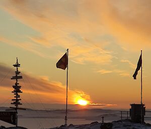 A sunrise from Casey with flags flying and the signpost in the foreground