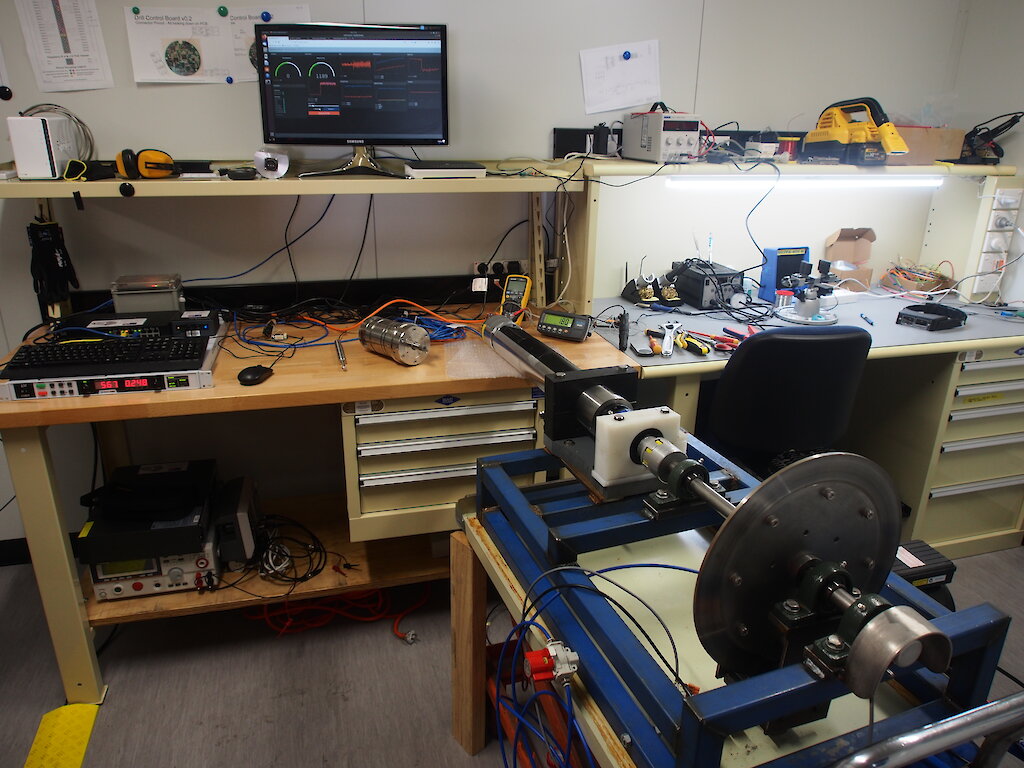 A cyclinder containing drill electronics attached to a brake pad to simulate drilling into ice, on a laboratory bench.