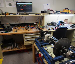 A cylinder containing drill electronics attached to a brake pad to simulate drilling into ice, on a laboratory bench.