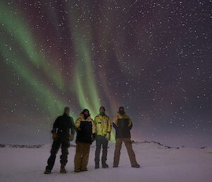 Four men standing on the ice with an Aurora Australis in the sky above