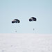 Two parachutes carrying small packages about to land on ice.