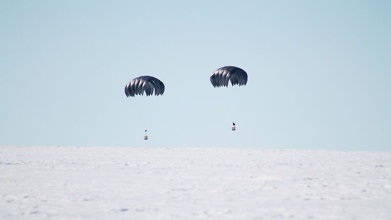 Two parachutes carrying small packages about to land on ice.