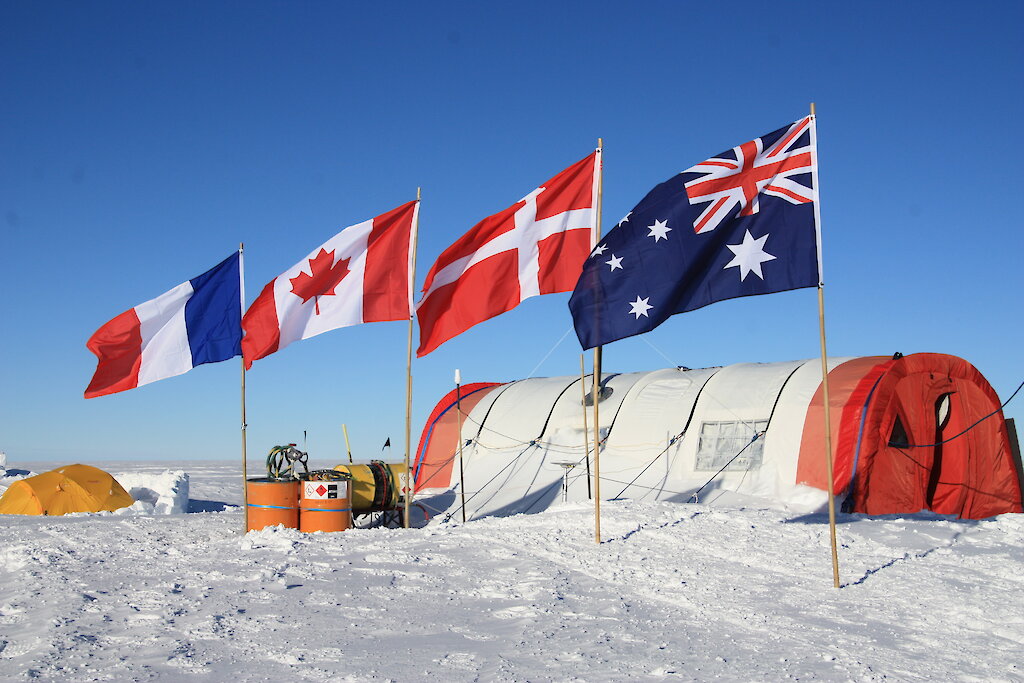 a white snow covered ground with four flags and a round tent in the background