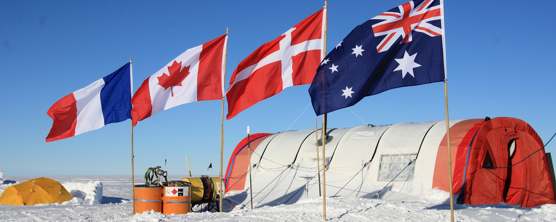 a white snow covered ground with four flags and a round tent in the background