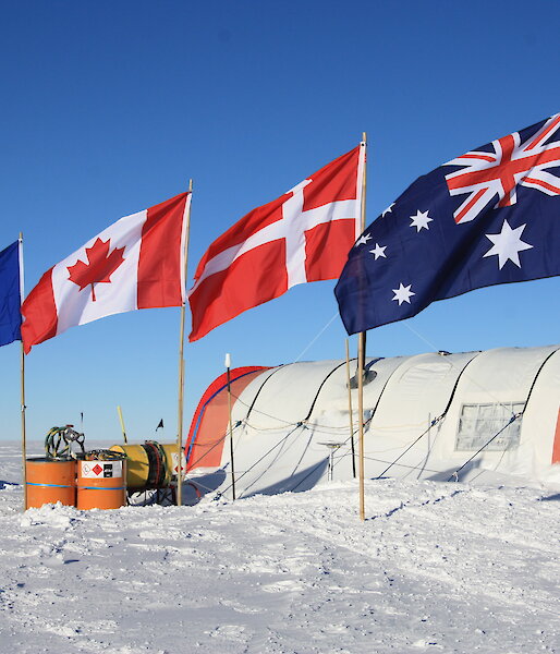 a white snow covered ground with four flags and a round tent in the background