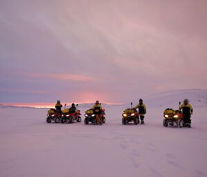 Five expeditioners on quad bikes on the sea ice, sunset in the background