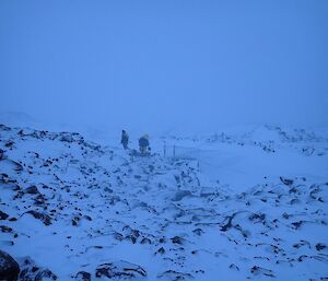 the gloomy winter light shows two expeditioners commencing the task of shovelling tonnes of compacted snow from the bridge