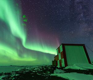 A bright green aurora streams across the sky above the old met building