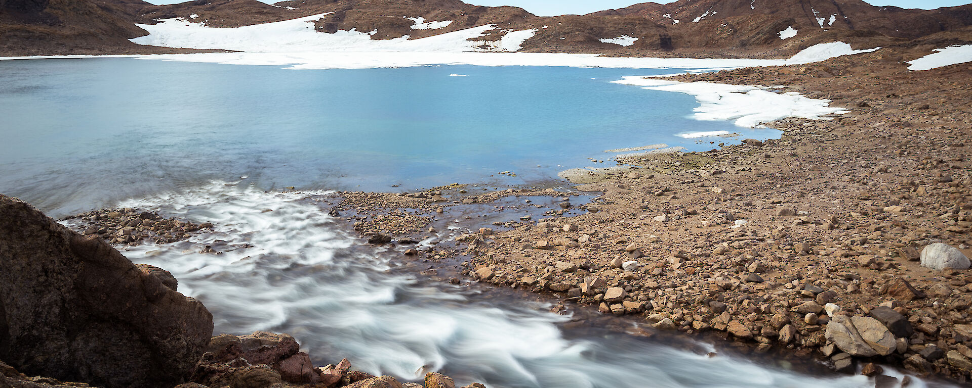 The blue and white Ellis Rapids flowing relentlessly into Ellis Fjord, surrounded by brown hills