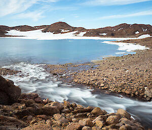 The blue and white Ellis Rapids flowing relentlessly into Ellis Fjord, surrounded by brown hills