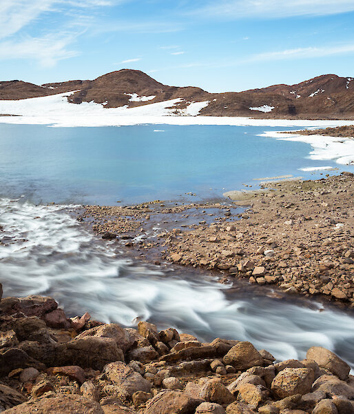 The blue and white Ellis Rapids flowing relentlessly into Ellis Fjord, surrounded by brown hills