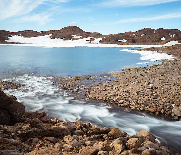 The blue and white Ellis Rapids flowing relentlessly into Ellis Fjord, surrounded by brown hills