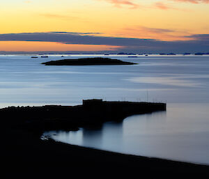 The wharf silhouetted against a still, blue bay and yellow midnight sky during summer