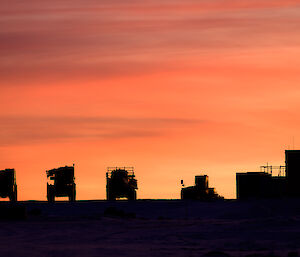 A red sunrise sky silhouettes the winterised cranes and trucks