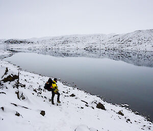 An expeditioners standing on the very snowy bank of a lake
