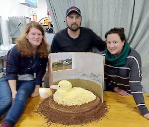 Three expeditioners pose behind a cake that resembles an albatross