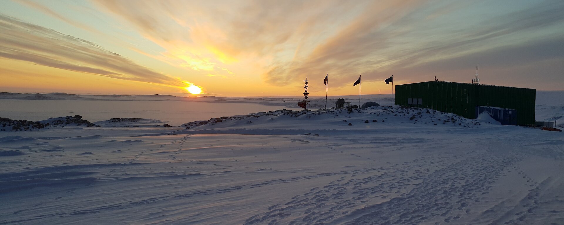 The sun rising in front of Casey station with the flags flying