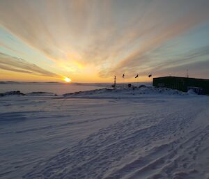 The sun rising in front of Casey station with the flags flying