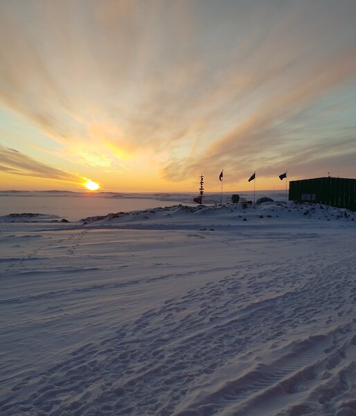 The sun rising in front of Casey station with the flags flying