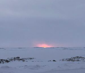 The sun glows pink through a thick cloud bank on the horizon