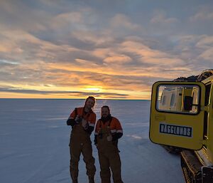 Two expeditioners stand next to a Hagg trip as the sunsets behind