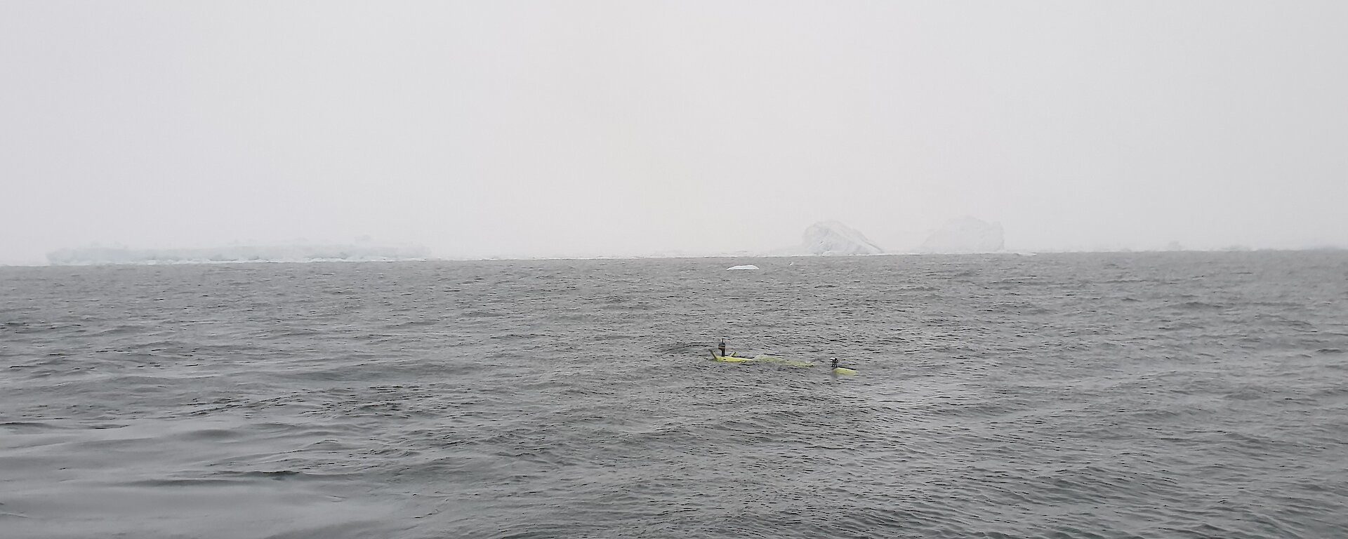 The AUV in a misty grey ocean with the Thwaites Glacier on the horizon.
