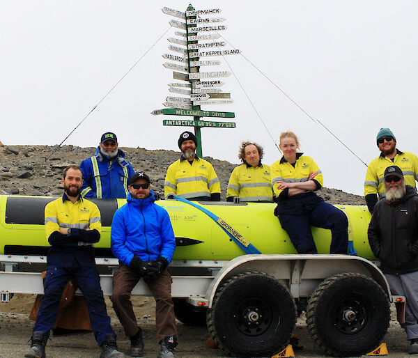Members of the AUV team at Davis research station standing beside the AUV on a trailer.