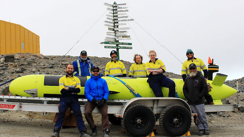 Members of the AUV team at Davis research station standing beside the AUV on a trailer.