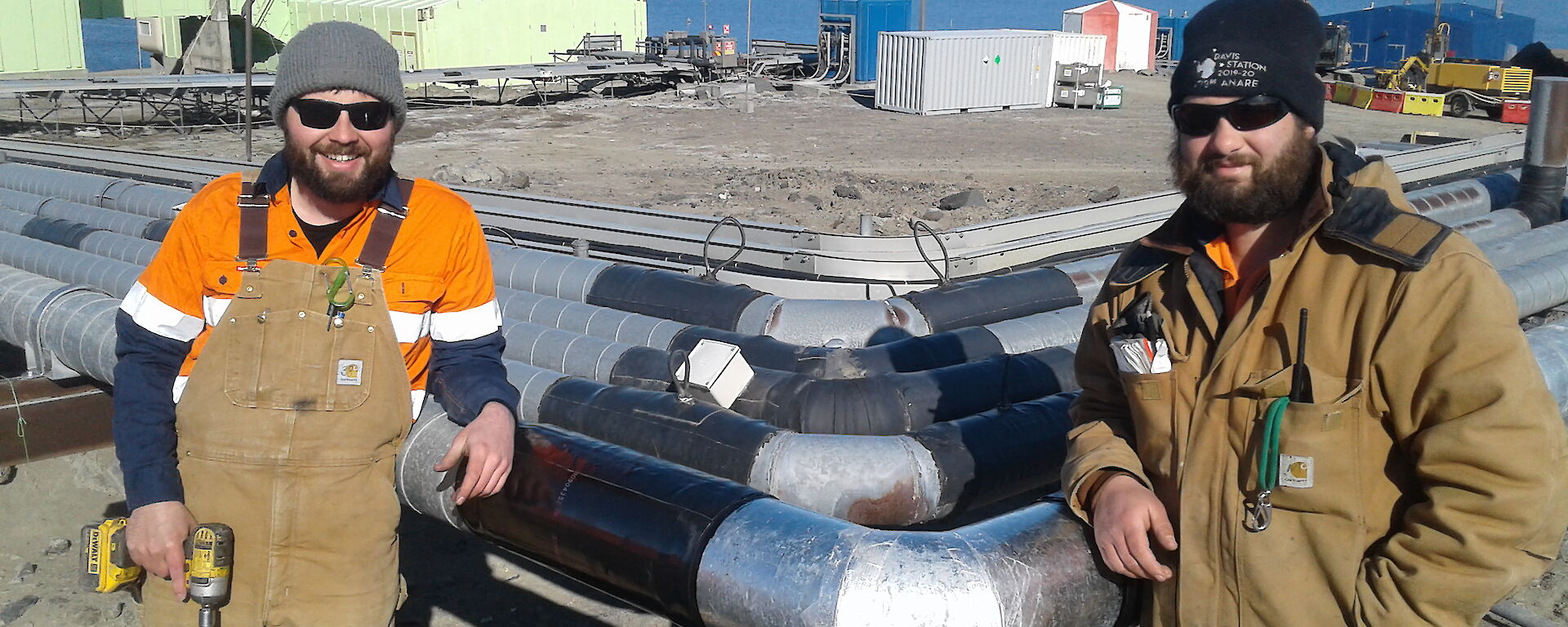 Two plumbers lean against site services pipes