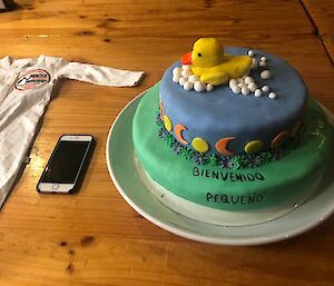 A baby onesie and a two tiered cake on the table