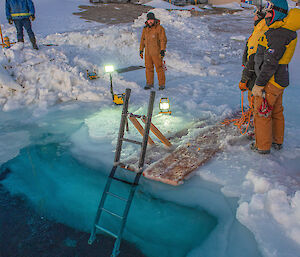 Australian expeditioners stand around a hole cut in the sea ice at Mawson research station as they prepare the ‘swimming pool’ for a midwinter dip