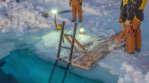 Australian expeditioners stand around a hole cut in the sea ice at Mawson research station as they prepare the ‘swimming pool’ for a midwinter dip