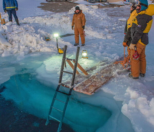 Australian expeditioners stand around a hole cut in the sea ice at Mawson research station as they prepare the ‘swimming pool’ for a midwinter dip