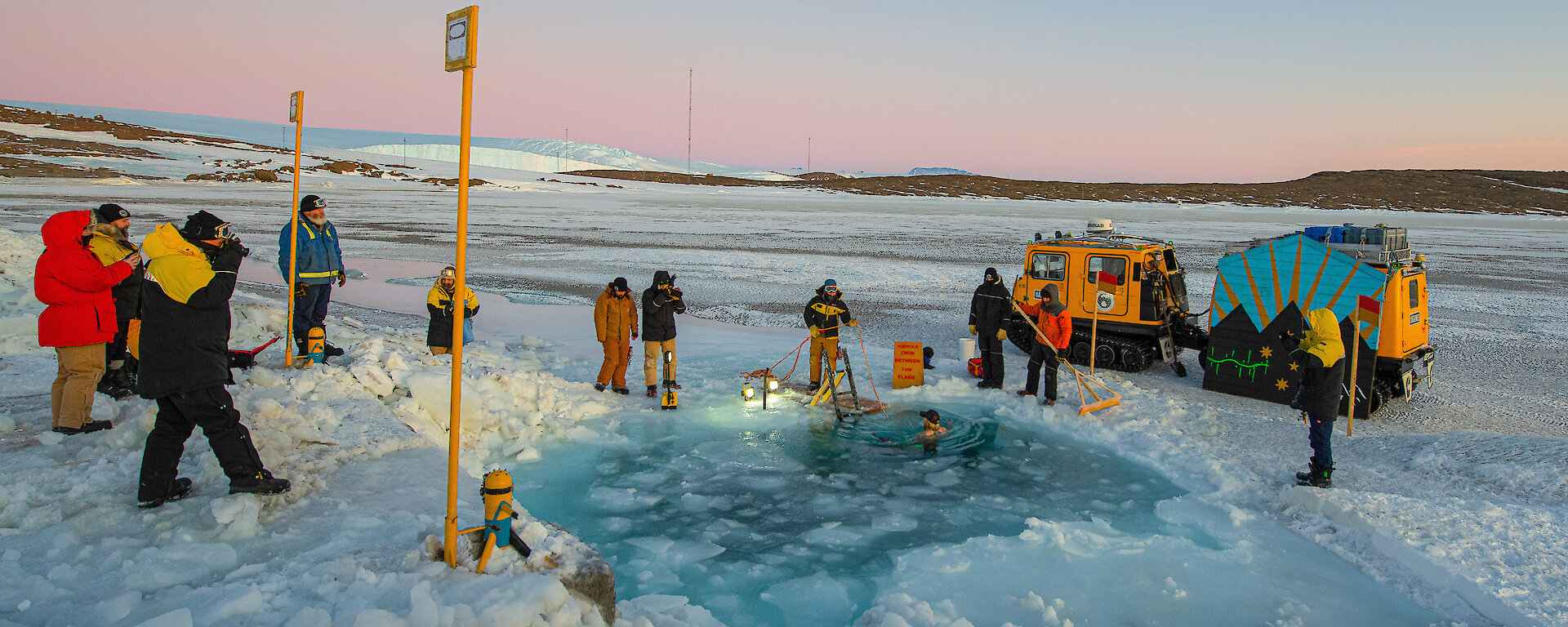 Mawson Station Leader, Matt Williams, takes an icy midwinter swim with his fellow wintering expeditioners watching on.