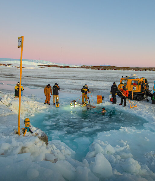 Mawson Station Leader, Matt Williams, takes an icy midwinter swim with his fellow wintering expeditioners watching on.