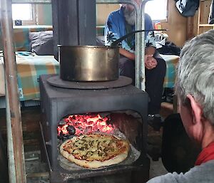 a pizza cooking in the oven at a field hut