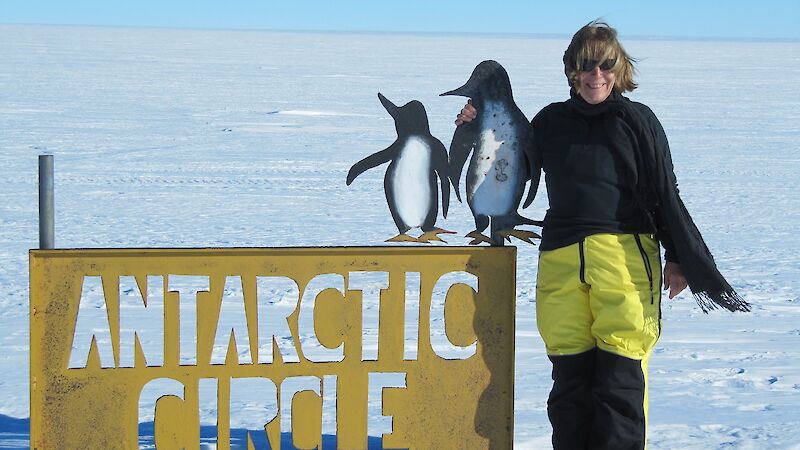 Woman stands on ice at Antarctic Circle sign.