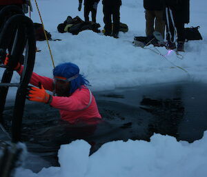 Expeditioner lowers himself into the icy swimming pool cut through the sea ice near Casey wharf.