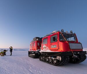 The red hagglunds sitting on the sea ice while a group measures sea ice thickness behind