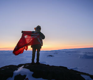 An expeditioner holding a flag while standing on top of a rock