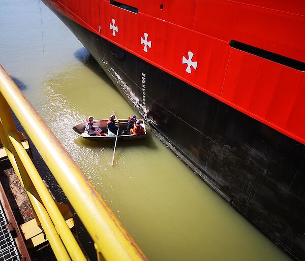 Men in a small row boat measure draft marks on the hull of the Nuyina.