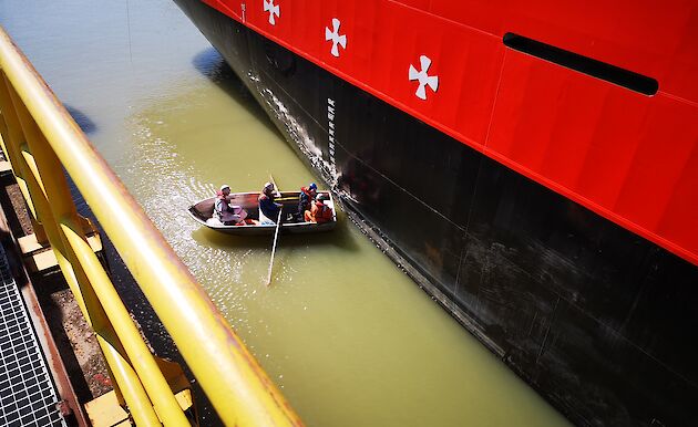 Men in a small row boat measure draft marks on the hull of the Nuyina.